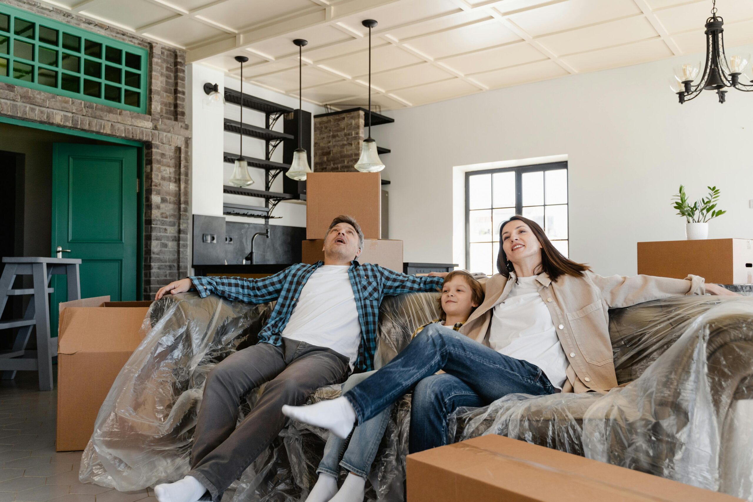 A family sits on a couch in a new home surrounded by moving boxes.